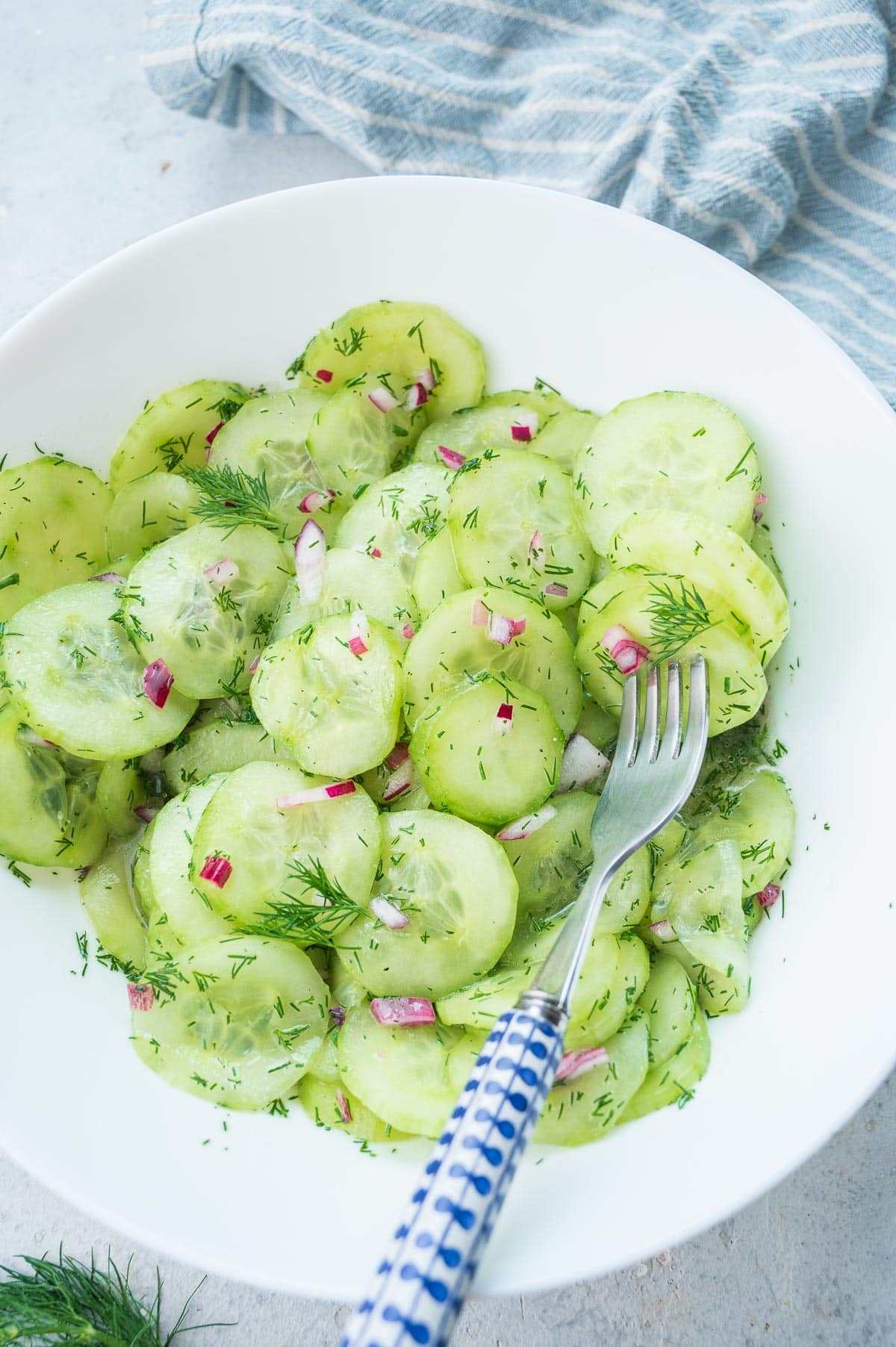 German cucumber salad in a white bowl with a fork on the side.